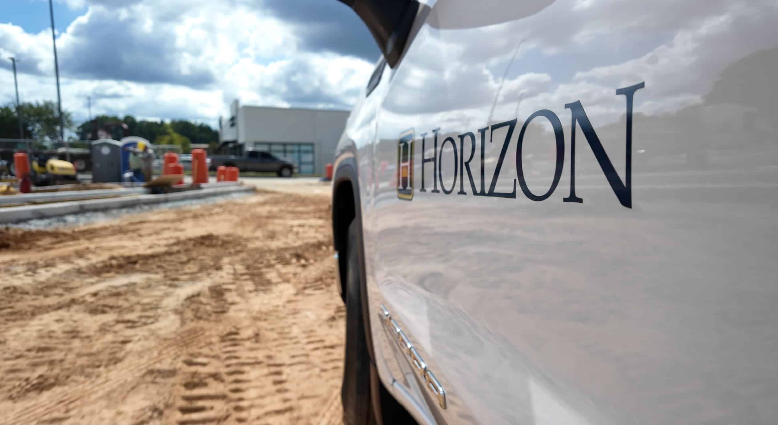 Side view of a white Horizon Construction pickup truck, driving onto an active construction site.